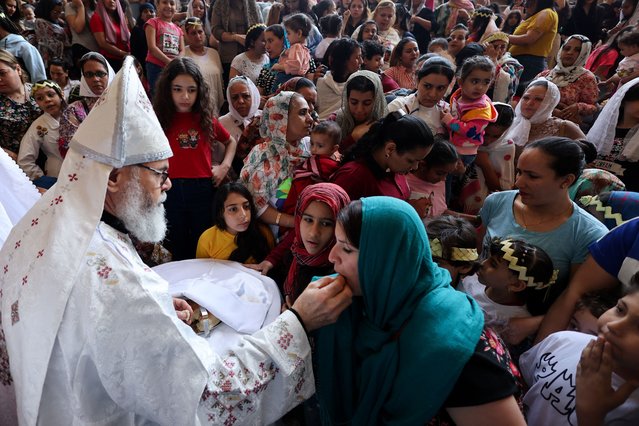 A Coptic Orthodox Christian priest gives communion to a woman during a Palm Sunday mass at the Samaan el-Kharaz Monastery in the Mokattam Mountain area of Cairo, Egypt, on April 28, 2024. (Photo by Amr Abdallah Dalsh/Reuters)