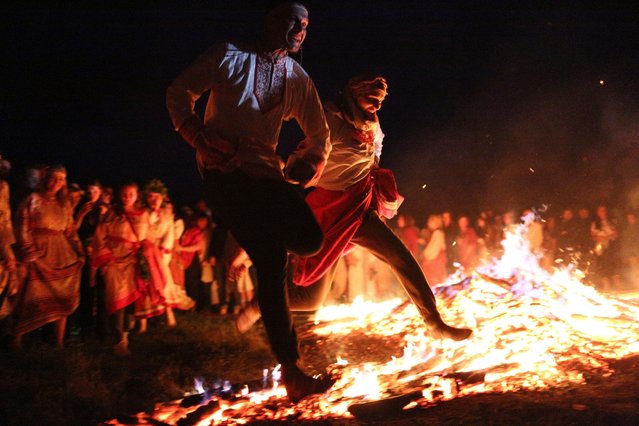 People jump over the fire wearing traditional Russian village-style clothes as they celebrate the summer solstice with a bonfire in the village of Okunevo, about 200 kilometers (125 miles) northeast of the Siberian city of Omsk, Russia, in Okunevo, Russia, late Thursday, June 20, 2024. (Photo by Evgeniy Sofiychuk/AP Photo)