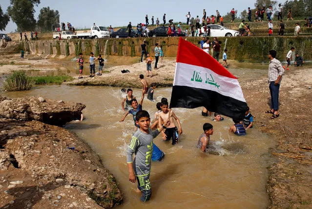 A boy holds the Iraqi flag as he plays in the water with other children during a Friday holiday at Shallalat district (Arabic for “waterfalls”) in eastern Mosul, Iraq, April 21, 2017. (Photo by Muhammad Hamed/Reuters)