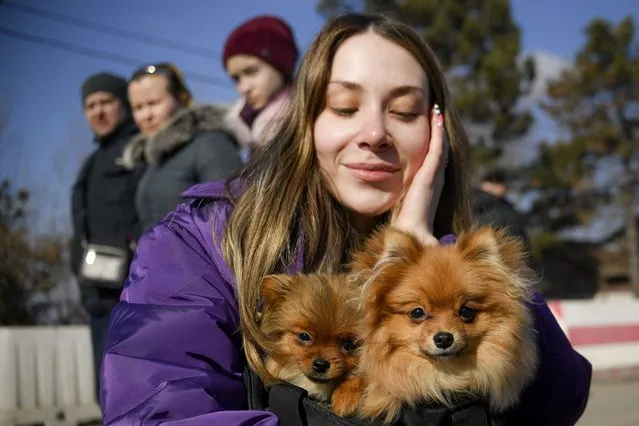 A refugee fleeing the war from neighbouring Ukraine holds two small dogs after crossing the border, at the Romanian-Ukrainian border, in Siret, Romania, Monday, March 14, 2022. (Photo by Andreea Alexandru/AP Photo)