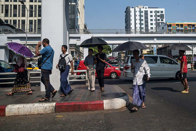 People walk under an umbrella to shelter from the sun during a heatwave in Yangon on April 2, 2024. (Photo by Sai Aung Main/AFP Photo)