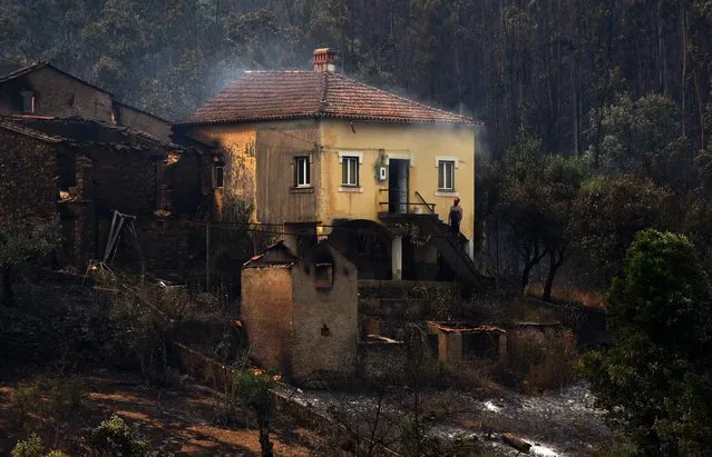 A man stands in the stairway of a house with smoke billowing from the roof in an area devastated by a wildfire in Canical, near Alvares, on May 18, 2017. A wildfire in central Portugal killed at least 57 people and injured 59 others, most of them burning to death in their cars, the government said on June 18, 2017. Several hundred firefighters and 160 vehicles were dispatched late on June 17 to tackle the blaze, which broke out in the afternoon in the municipality of Pedrogao Grande before spreading fast across several fronts. (Photo by Miguel Riopa/AFP Photo)