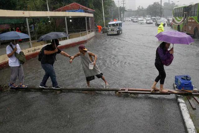 Commuters cross on a wooden plank for a fee to avoid a flooded street after heavy rains brought about by tropical storm “Nesat” flooded some parts of metropolitan Manila Thursday, July 27, 2017 in Manila, Philippines. The Philippine Atmospheric, Geophysical and Astronomical Services Administration (PAGASA) said the storm was packing maximum sustained winds of 85 kilometers per hour (53 miles per hour) in northeastern Philippines and is not expected to hit land but will enhance the southwest monsoon which will bring heavy rains over a wide section of the country. Classes have been suspended in different parts of Metro Manila and nearby provinces Thursday. (Photo by Bullit Marquez/AP Photo)