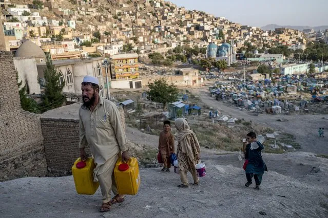 People carry drinking water in containers as they walk along a hillside near the Kart-e-Sakhi cemetery in Kabul on July 18, 2022. (Photo by Wakil Kohsar/AFP Photo)