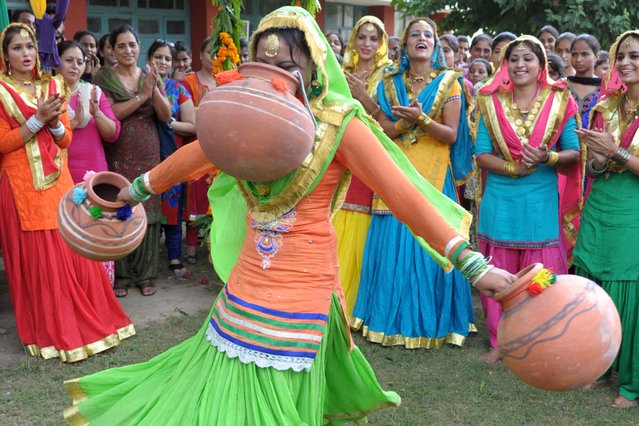 Young Indian women wearing traditional Punjabi dress look on as one dances the “giddha” during Teej festival celebrations on the occasion of Sawan (rain) Month at Shahzada Nand College in Amritsar on August 8, 2014. The Teej festival heralds the rainy season and is especially popular with women and revolves around dressing in finery and singing and dancing. (Photo by Narinder Nanu/AFP Photo)