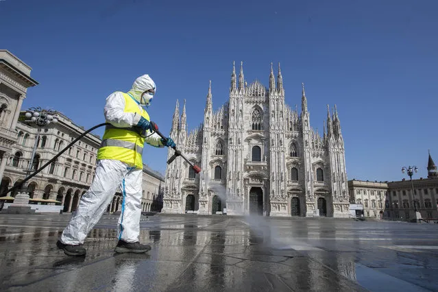 A worker sprays disinfectant to sanitize Duomo square, as the city main landmark, the gothic cathedral, stands out in background, in Milan, Italy, Tuesday, March 31, 2020. (Photo by Luca Bruno/AP Photo)