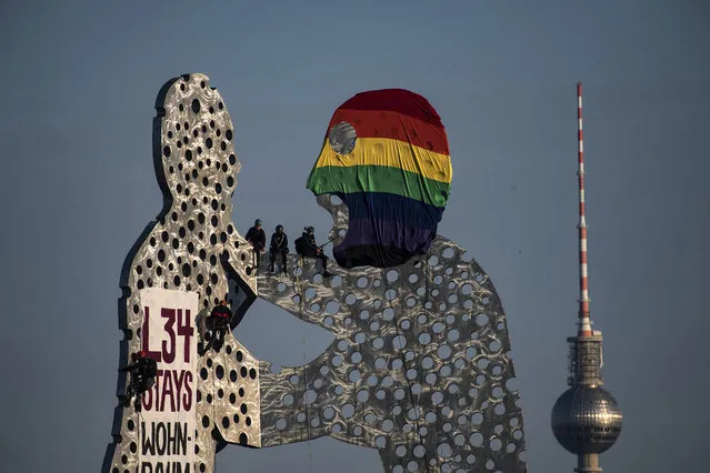 Activists occupy the Molecule Man sculpture to draw attention to Liebig 34, a squat and collective in the district of Friedrichshain, which is threatened by eviction in Berlin, Germany on July 14, 2020. One of the figures was put on a balaclava in rainbow colours by several climbers. (Photo by Paul Zinken/AP Photo/dpa)