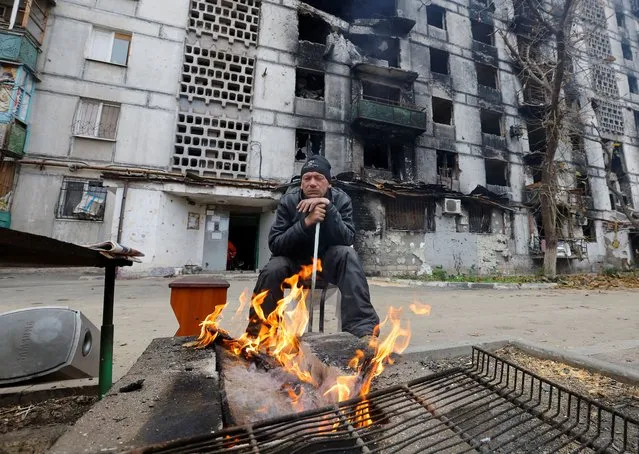 A local resident sits by the fire outside an apartment building heavily damaged in the course of Russia-Ukraine conflict, in Mariupol, Russian-controlled Ukraine on November 16, 2022. (Photo by Alexander Ermochenko/Reuters)