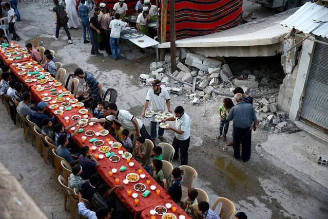 People gather for Iftar (breaking fast), organised by Adaleh Foundation, amidst damaged buildings during the holy month of Ramadan in the rebel-held besieged town of Douma to the east of Damascus, Syria, June 18, 2017. (Photo by Bassam Khabieh/Reuters)
