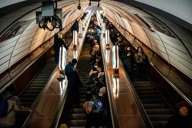 Civilians sit on an escalator while take shelter inside a metro station during an air raid alert in the centre of Kyiv on December 16, 2022, amid the Russian invasion of Ukraine. A fresh barrage of Russian strikes hit cities across Ukraine early on December 16, 2022 cutting water and electricity in major cities and piling pressure on Ukraine's grid with temperatures below freezing. (Photo by Dimitar Dilkoff/AFP Photo)