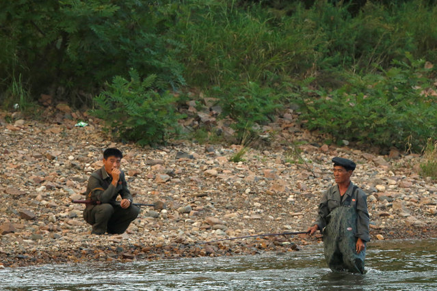 A North Korean soldier squats near man who is fishing in the Yalu River, outside the North Korean town of Sinuiju, opposite Dandong in China's Liaoning province, September 11, 2016. (Photo by Thomas Peter/Reuters)