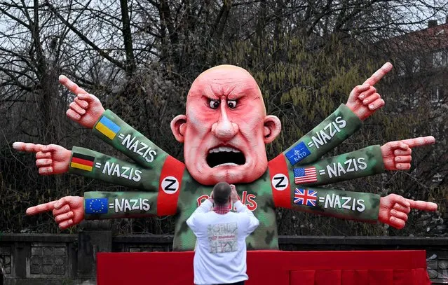 A man takes pictures of a carnival float featuring Russian oligarch Yevgeny Viktorovich Prigozhin, co-founder of the Russian state-backed mercenary company Wagner Group, who has six arms with the flags of Ukraine, Germany, Europe, NATO, the US and Britain, equating them all with nazis, during a Rose Monday street carnival parade in Duesseldorf, western Germany, on February 20, 2023. (Photo by Ina Fassbender/AFP Photo)