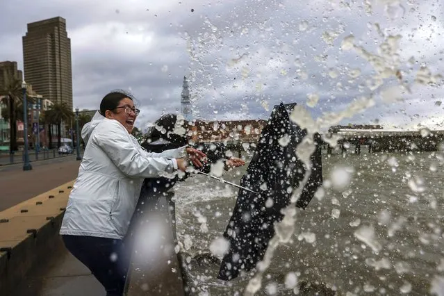 Dulce Gonzalez, 19, left, and sister Nathalie Gonzalez, 15, joke around while the waves crash along the Embarcadero during a rainstorm in San Francisco, California on Wednesday, January 4, 2023. (Photo by Gabrielle Luri/San Francisco Chronicle via AP Photo)