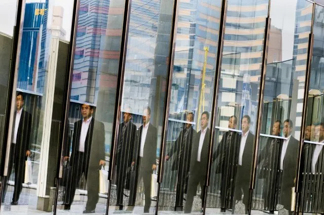 Men are reflected in a glass railing as they walk at the Shiodome business district in Tokyo November 12, 2014. Japanese companies overwhelmingly want Prime Minister Shinzo Abe to delay or scrap a planned tax increase, a Reuters poll shows, highlighting concerns that it could derail a fragile economic recovery. (Photo by Thomas Peter/Reuters)