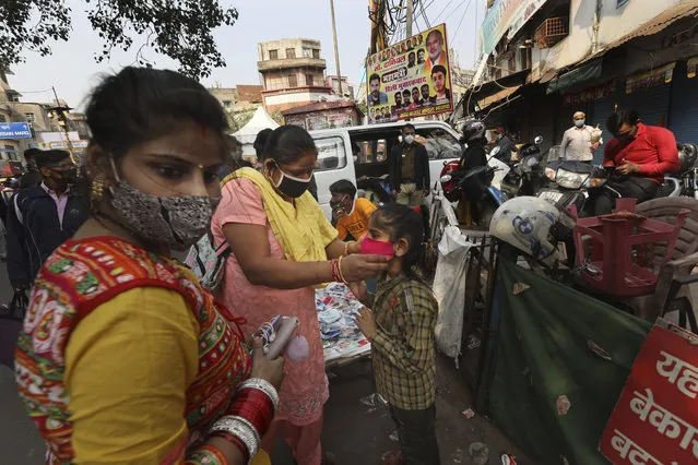 A woman puts on a face mask on her daughter at a market place in New Delhi, India, Thursday, November 19, 2020. (Photo by Manish Swarup/AP Photo)