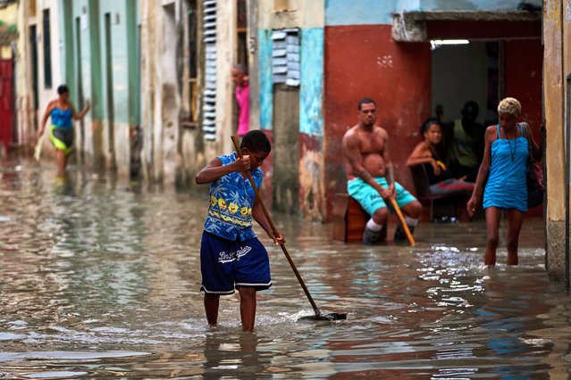 A youth sweeps away trash blocking drains on a flooded street after heavy rains in Havana, Monday, August 11, 2025. (Photo by Ramon Espinosa/AP Photo)