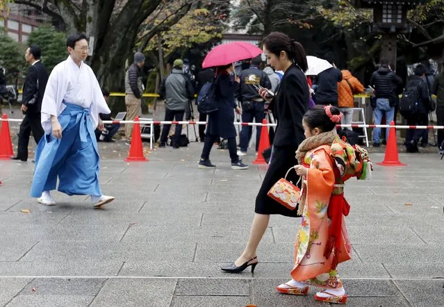 A girl wearing a Kimono visits Yasukuni shrine to celebrate Shichi-Go-San and walks past journalists who stand near the site of an explosion at the Yasukuni shrine in Tokyo, Japan, November 23, 2015. Shichi-Go-San is a traditional Japanese rite-of-passage for three and seven-year-old-girls and three and five-year-old-boys celebrating their well-being. (Photo by Toru Hanai/Reuters)