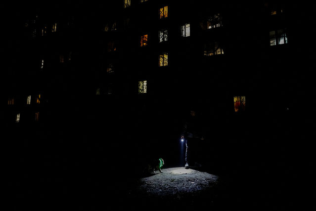 A man uses a torch light to take his dog for a walk during partial power-cuts, amid Russia's attack on Ukraine, in Kyiv, Ukraine on November 28, 2024. (Photo by Alina Smutko/Reuters)