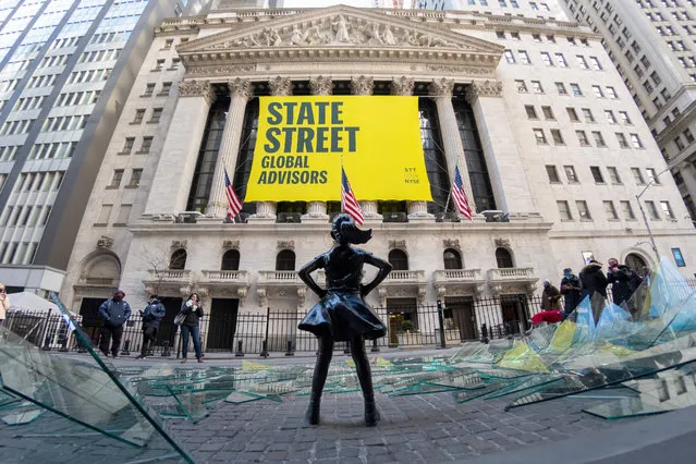 People walk past a broken glass ceiling installation in front of the Fearless Girl Statue in front of the New York Stock Exchange on International Women's Day on March 08, 2021 in New York City. The art installation by Global Street Global Advisors celebrates women who have made a difference for all “Fearless Girls”. (Photo by Alexi Rosenfeld/Getty Images)