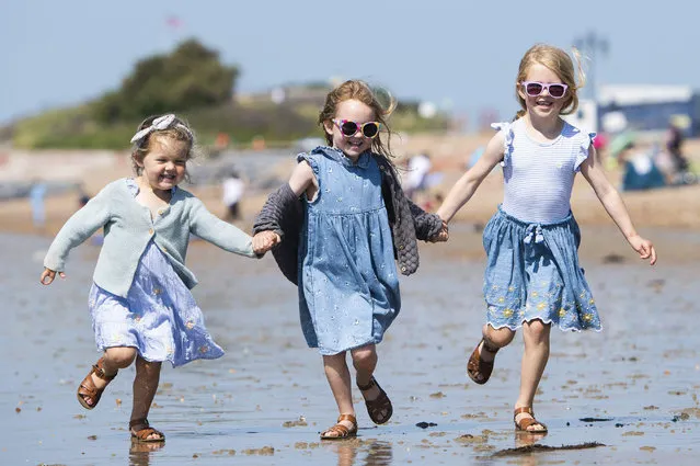 Sisters Rose four, Jessie, five, and Elodie Lanbert, six, get their matching sandals wet in Southsea, Hampshire in South East England on June 25, 2023. (Photo by Will Dax/Solent News)