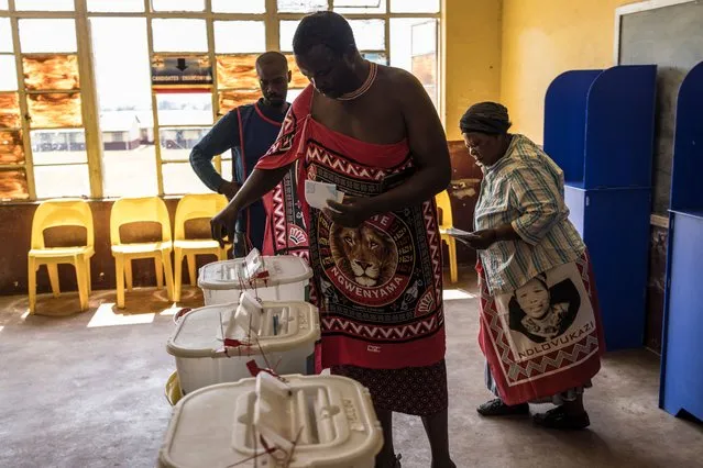 A voter wearing the traditional emahiya attire casts his ballot next to a woman wearing a traditional lihiya attire printed with the portrait of Queen Ndlovukazi, mother of King Mswati III, during Eswatini's parliamentary elections at a voting station at the National High School in Lobamba, on September 29, 2023. (Photo by Marco Longari/AFP Photo)