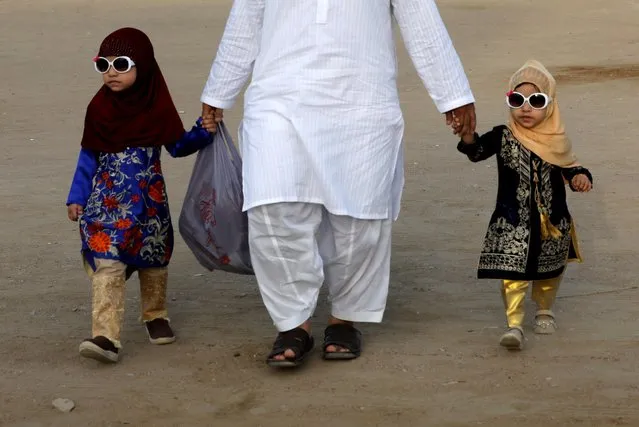 Siblings along with their father walk after celebrating Eid al-Fitr prayers to mark the end of the holy fasting month of Ramadan, as the outbreak of the coronavirus disease (COVID-19) continues in Karachi, Pakistan on May 13, 2021. (Photo by Akhtar Soomro/Reuters)