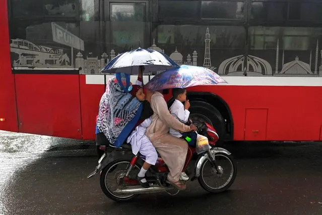 A family rides a bike amid rain in Lahore on October 16, 2023. (Photo by Arif Ali/AFP Photo)