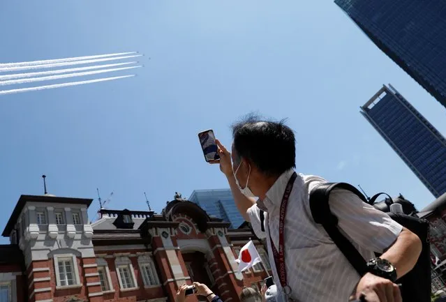 A man takes a picture as Japan's aerobatics team, the Blue Impulse, perform during a practice run for the opening ceremony over the Tokyo 2020 Olympic Games countdown clock on July 21, 2021. (Photo by Androniki Christodoulou/Reuters)
