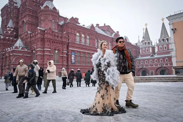 A couple of Malaysian tourists poses on the edge of Red Square as snow falls in Moscow on November 23, 2023. (Photo by Natalia Kolesnikova/AFP Photo)