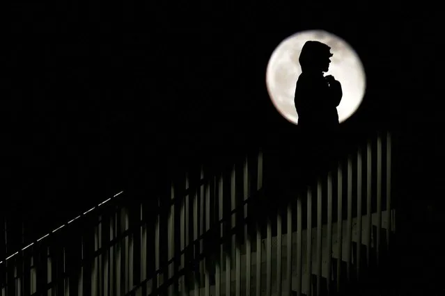A person is silhouetted in front of an almost full moon in Tirana, Albania on December 28, 2023. (Photo by Florion Goga/Reuters)
