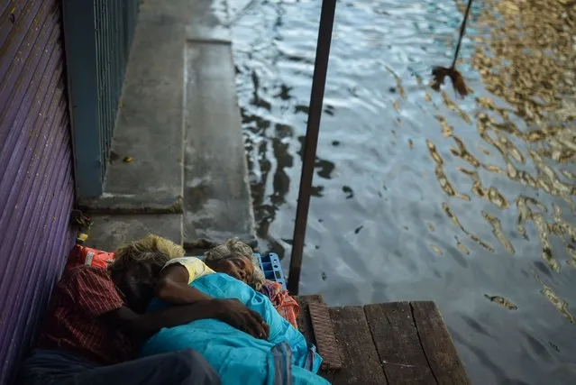An elderly couple sleeps on the stairs of a closed shop in a flooded neighborhood following incessant heavy rains, in Chennai, India, 12 November 2021. The India Meteorological Department (IMD) has lifted the red alert for extremely heavy rains in Chennai as the low pressure over northern coastal Tamil Nadu weakened to a well-developed depression. Tamil Nadu reports 14 deaths due to heavy rains and flooding in several places. According to the new report by the Intergovernmental Panel on Climate Change (IPCC), major coastal cities such as Mumbai, Kochi, Visakhapatnam and Chennai may be up to three feet under water by the end of the century. More than 200 scientists called on the U.N. Climate Summit COP 26 on November 11, 2021, to take immediate action to halt global warming, warning in an open letter that some climate change impacts are irreversible for generations. (Photo by Idrees Mohammed/EPA/EFE)