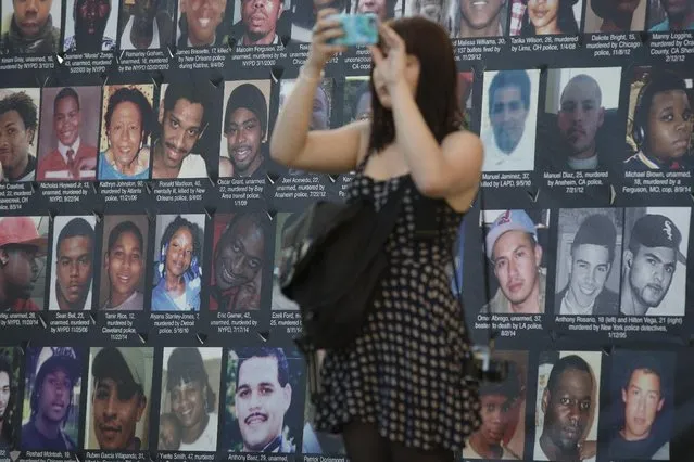 A pedestrian takes a photo of demonstrators as they march during a protest against the acquittal of Michael Brelo, a patrolman charged in the shooting deaths of two unarmed suspects, Saturday, May 23, 2015, in Cleveland. (Photo by John Minchillo/AP Photo)