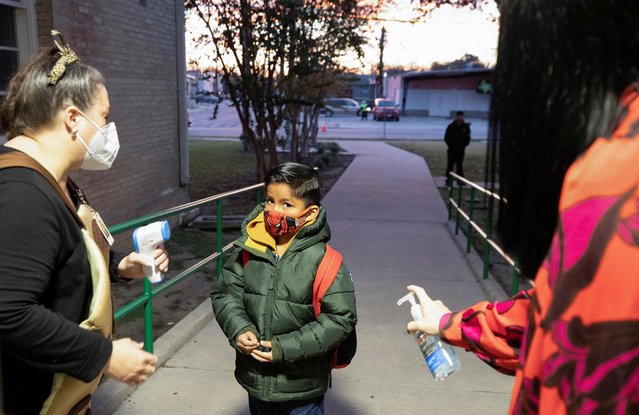 Andrew Briscoe Elementary School Principal Jennifer Emerson greets and distributes hand sanitizer to students with another teacher taking their temperature before they enter the building in San Antonio, Texas, January 11, 2022. (Photo by Kaylee Greenlee Beal/Reuters)