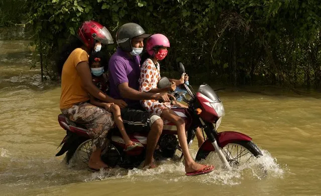 A Sri Lankan family rides a motorcycle past a flooded area in Gampaha, about 20 kilometres east of Colombo, Sri Lanka, Wednesday, November 10, 2021. At least 16 people have died in floods and mudslides in Sri Lanka following more than a week of heavy rain, officials said Wednesday. (Photo by Eranga Jayawardena/AP Photo)