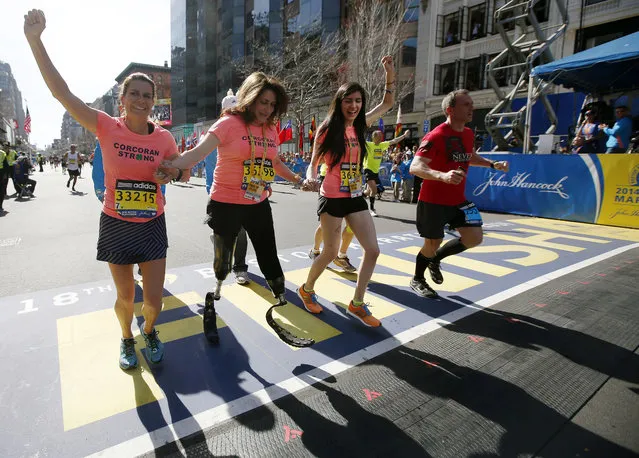 Double amputee Celeste Corcoran, center, a victim of last year's bombings, reaches the finish line of the 118th Boston Marathon, Monday, April 21, 2014, in Boston, with the aid her sister Carmen Acabbo, left, and daughter Sydney, right, who was also wounded last year. (Photo by Elise Amendola/AP Photo)