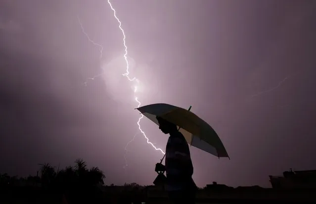 A pedestrian walks with an umbrella as lightning strikes during an evening thunderstorm in Jammu, India on May 14, 2015. (Photo by Rakesh Bakshi/AFP Photo)