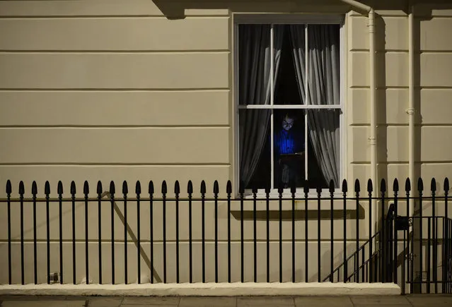 A man is illuminated by his tablet as he stands by his window on a warm spring evening in Westminster, London, May 11, 2015. (Photo by Dylan Martinez/Reuters)