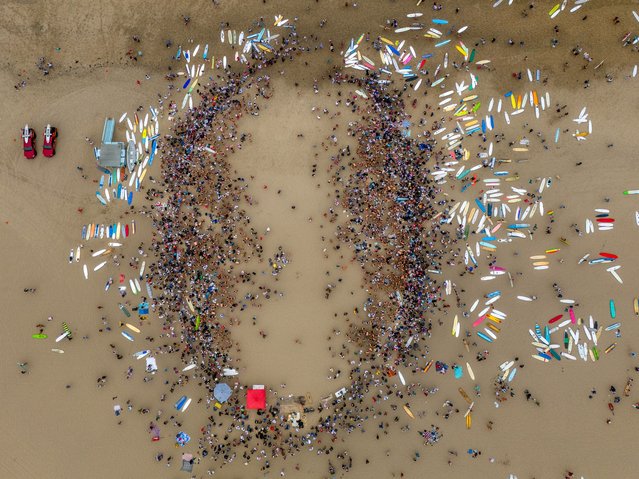 In an aerial view, surrounded by paddle and surf boards, hundreds of people gather to drink beer during the final of three stages of the annual Hermosa Ironman July 4, 2024 in Hermosa Beach, California. The loose competition involves contestants running a mile, paddling a mile and chugging a six-pack of beer. (Photo by Jay L. Clendenin/Getty Images)