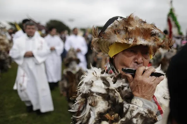 Pedro Balbuena plays the harmonica as walks ahead of the procession marking the feast day of St. Francisco Solano in Emboscada, Paraguay, Friday, July 24, 2015. Balbuena is seen as the chief of the feathered-ones. He says he has been organizing the dancing performance honoring St. Francis for 40 years. His group includes children, adults and the elderly. They practice for three months and they prefer to use rooster feathers for the suits, because they're more colorful. (Photo by Jorge Saenz/AP Photo)