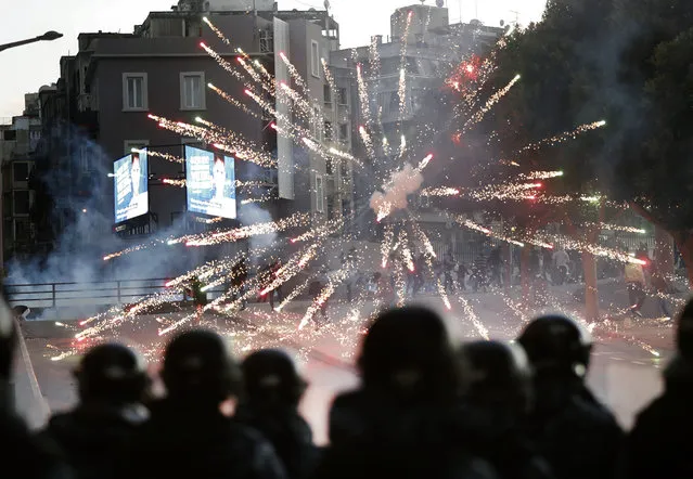 Supporters of the Shiite Hezbollah and Amal Movement groups, background, fire firecrackers against the riot policemen, foreground, as they try to attack the anti-government protesters squares, in downtown Beirut, Lebanon, Saturday, December 14, 2019. Lebanon has been facing its worst economic crisis in decades, amid nationwide protests that began on Oct. 17 against the ruling political class which demonstrators accuse of mismanagement and corruption. (Photo by Hussein Malla/AP Photo)