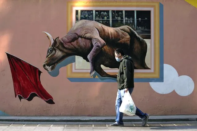 A man wearing a face mask to help protect from the coronavirus carries a bag of groceries as he walks by a mural depicting an iconic financial market bull statue near the central business district, Monday, April 18, 2022, in Beijing. China’s economic growth edged up to a still-weak 4.8% over a year earlier in the first three months of 2022 as spreading coronavirus outbreaks prompted shutdowns of major industrial cities. (Photo by Andy Wong/AP Photo)