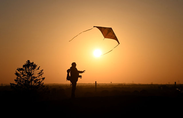 A man who lets fly his kite silhouettes against a golden sky as sun sets behind the Olympic park in Munich, southern Germany, at the end of a sunny late summer day on September 18, 2024. (Photo by Michaela Stache/AFP Photo)