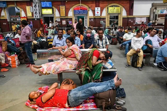 Passengers take rest and wait at a train station due to delay and rescheduling of a few trains after the rail network was damaged in some parts of the country following protests against the government's new 'Agnipath' recruitment scheme for the army, navy, and air forces, at the Howrah railway station in Kolkata on June 20, 2022. (Photo by Dibyangshu Sarkar/AFP Photo)