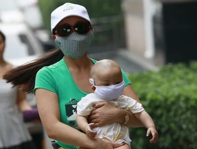 A woman carrying a baby, both wearing masks, make their way down a street in Binhai new district, more than five kilometers (3 miles) away from the site of last week's explosions, in Tianjin, China, August 17, 2015. (Photo by Kim Kyung-Hoon/Reuters)