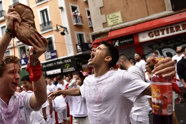 A reveler drinks from a wineskin while waiting for the launch of the “Chupinazo” rocket, to mark the official opening of the 2022 San Fermin fiestas in Pamplona, Spain, Wednesday, July 6, 2022. The blast of a traditional firework opens Wednesday nine days of uninterrupted partying in Pamplona's famed running-of-the-bulls festival which was suspended for the past two years because of the coronavirus pandemic. (Photo by Alvaro Barrientos/AP Photo)