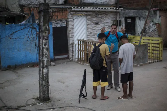 In this July 16, 2016 photo, pastor Nilton blesses two young drug traffickers at a slum in Rio de Janeiro, Brazil. Many of the young drug traffickers have an immense respect for the pastor, a former drug trafficker. It's not uncommon to see young men set their weapons down, but only long enough to receive his blessing. (Photo by Felipe Dana/AP Photo)