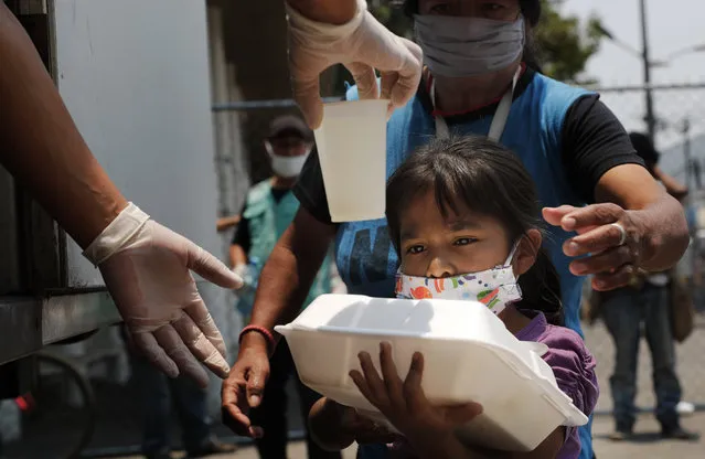 A child gets a meal from the mobile dining rooms program as people who have not been able to work because of the COVID-19 pandemic line up for a meal outside the Iztapalapa hospital in Mexico City, Wednesday, May 20, 2020. (Photo by Marco Ugarte/AP Photo)