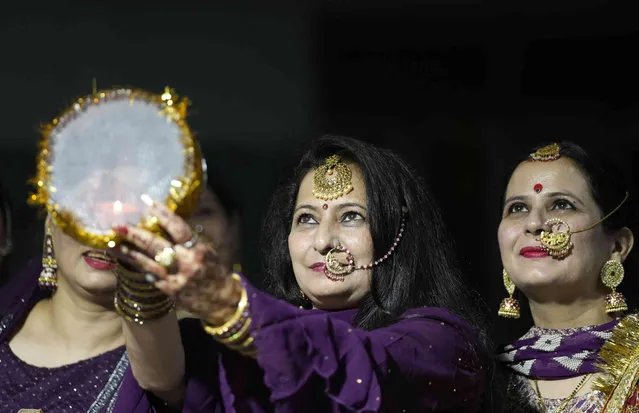 Married Hindu women look at the moon through a sieve as part of a ritual to break her fast during Karva Chauth festival in Jammu, India, Thursday, October 13, 2022. Hindu married women decorate their hands with henna, wear colorful bangles and observe a fast to pray for the longevity and well being of their husbands during this festival. (Photo by Channi Anand/AP Photo)