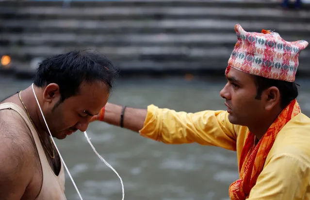 A Hindu priest (R) offers a new sacred thread to a devotee during the Janai Purnima (Sacred Thread) Festival at Pashupatinath temple in Kathmandu, Nepal, August 18, 2016. (Photo by Navesh Chitrakar/Reuters)