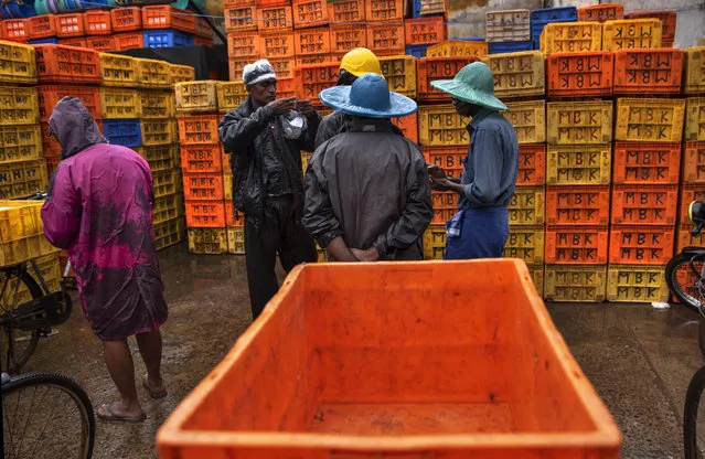 A man prepares to wear his mask as fish vendors chat on a rainy day in Kochi, Kerala state, India, Monday, June 22 2020. India is the fourth hardest-hit country by the COVID-19 pandemic in the world after the U.S., Russia and Brazil. (Photo by R.S. Iyer/AP Photo)